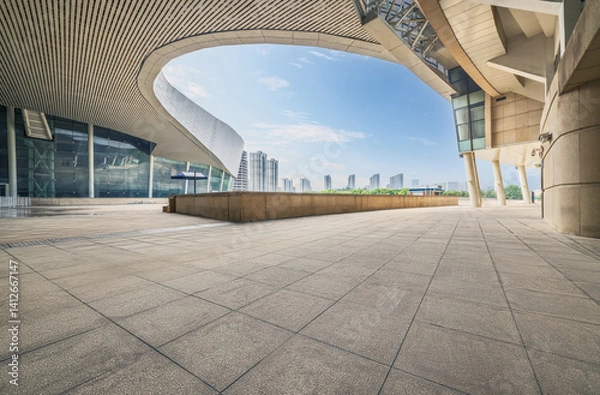 Fototapeta Empty floor square beside modern curved architectural building with city skyline background on a sunny day.