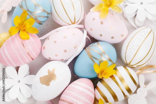 Fototapeta Pastel Easter eggs with gold decor and yellow flowers arranged in soft light. Festive flat lay for spring celebrations, Easter promotions, seasonal design and holiday greeting card templates