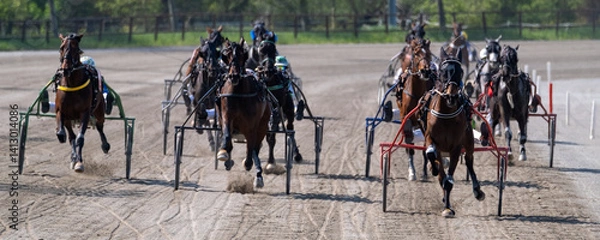 Obraz Modena, Italy – 04 09 2025: Racing horses trots and rider on a track of stadium. Competitions for trotting horse racing. Horses compete in harness racing. Horse runing at the track with rider.
