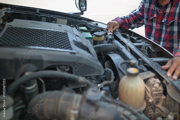 Fototapeta The man is checking the engine and condition of car to fix it properly and safely before traveling long distances. The man is checking condition of the car and the engine before traveling for safety.