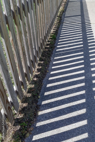 Fototapeta Picket fence with shadows on sidewalk