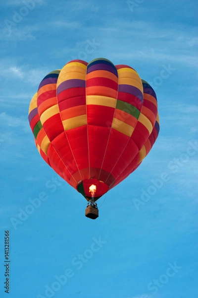 Fototapeta A colorful bright hot air balloon in the blue sky with a fire in the basket heating the air in the dome