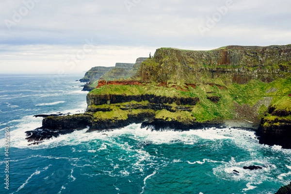 Obraz Dramatic Aerial of Giant’s Causeway Cliffs With Crashing Blue Waves During a Cloudy Day