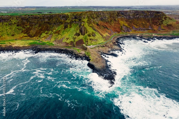 Obraz Moody Aerial View of Giant’s Causeway With Waves Crashing Into the Rocks and People Walking Around	