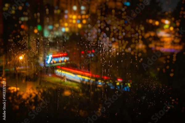 Obraz Rain covered glass with colorful night city lights in dreamy bokeh. Rain and bokeh create autumn mood. City lights blur in raindrops on window, nighttime in urban landscape, vivid blur in background