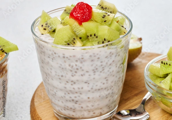 Fototapeta Yogurt and chia seed pudding in a glass, kiwi pieces. White table