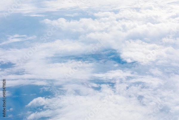 Obraz An aerial view reveals a vast expanse of fluffy white clouds floating over a serene blue sky. Ethereal scene, with hints of the earth below, is perfect for atmospheric theme