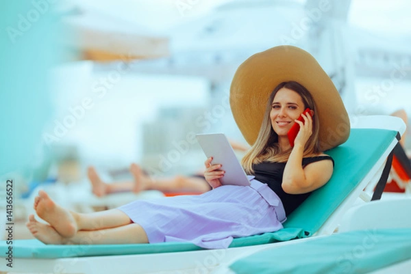 Fototapeta Woman at the Seaside on a Sunbed Working on Tablet and Phone. Person who works remotely on vacation because she is a workaholic