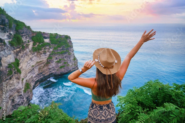 Obraz Traveler girl wearing hat enjoys turquoise stunning ocean view on cliff during traveling at beautiful destination on Bali island, Indonesia
