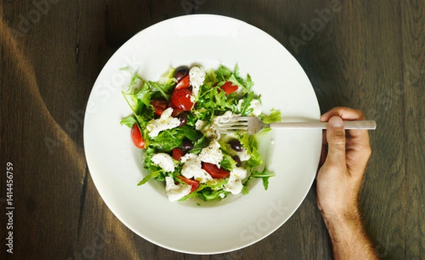 Fototapeta Hand with fork on plate with healthy green salad , top view