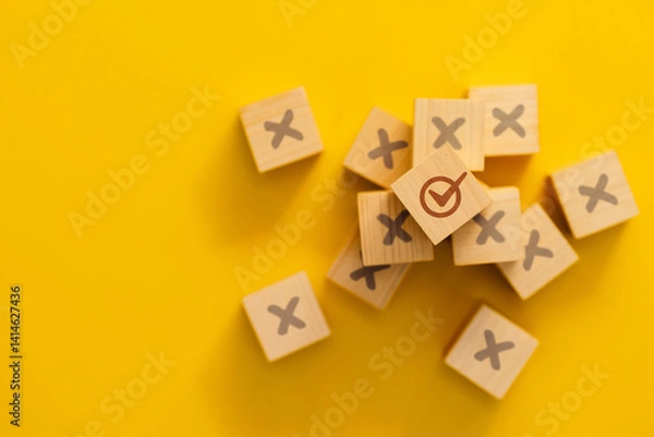 Obraz A wooden cube on a yellow background, with one block having a check mark out of many, with an X sign, representing a correct choice or success.