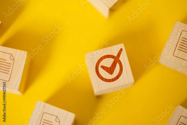 Obraz A close-up of a single wooden cube with a red check mark, placed on a bright yellow background, representing a choice or correctness.