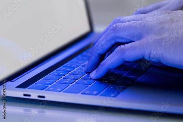 Fototapeta Hes got his finger on the trigger.An unrecognizable male gamer playing video games with blue laptop in a dark room at home.