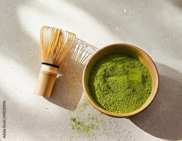 Fototapeta Bowl of matcha powder on light background with bamboo whisk and soft shadows.