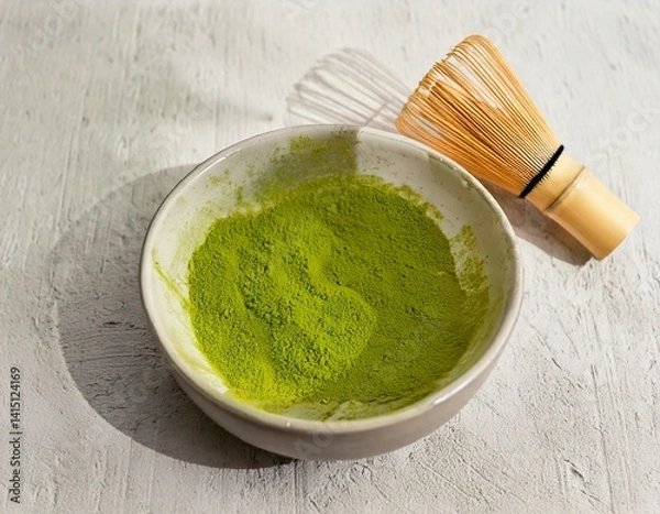 Fototapeta Bowl of matcha powder on light background with bamboo whisk and soft shadows.