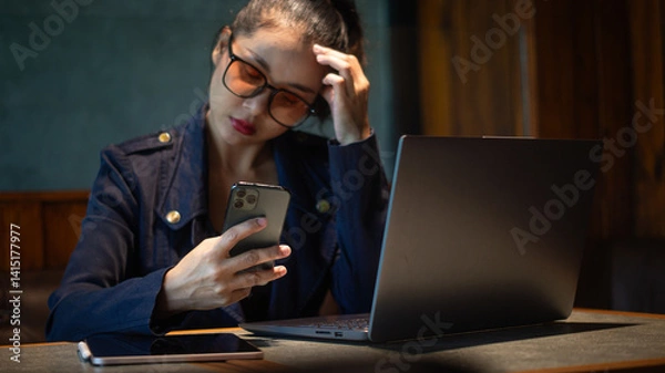 Obraz Businesswoman stressed out at work and tracking investment prices on smartphone in hand with laptop and tablet on desk.