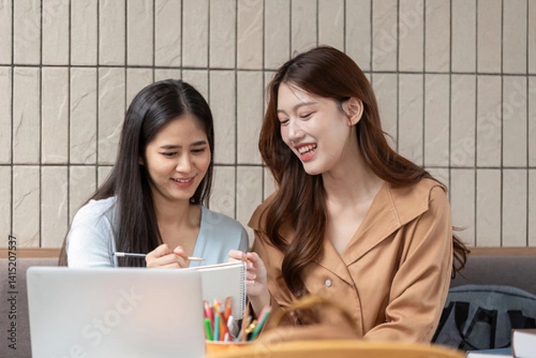 Fototapeta Collaboration and Engagement. Two students laughing together while reviewing their notes and study materials.
