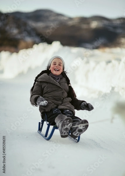 Obraz A girl laughs while sledding in winter