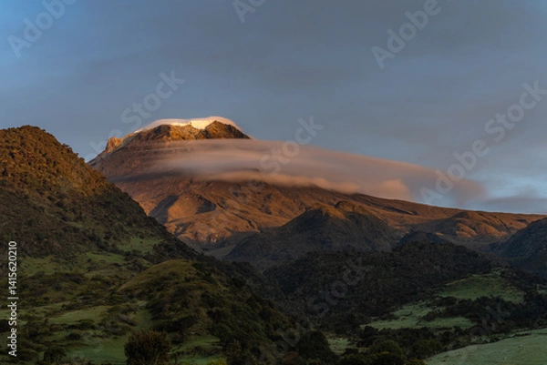 Fototapeta View of snow-capped volcano at sunrise with a cloud under the ice on a Colombian farm, with natural colors in gold. Colombian Andes Nevado del Tolima