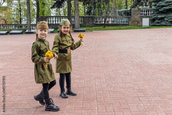 Fototapeta Patriotic education of youth. Little girls in an old Soviet military uniform laying flowers at the eternal flame near the monument to fallen soldiers in world War II. Victory Day on May 9. Copy space