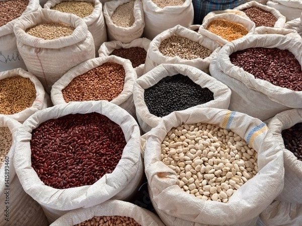 Fototapeta Top view of various types of beans, lentils, and grains in large white fabric sacks arranged closely together at an outdoor local market. Natural dry food assortment for sale.