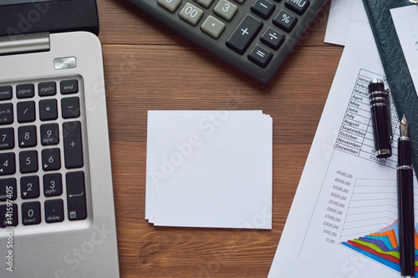 Fototapeta Financial printed paper charts, graphs, diagrams, computer, pen, and calculator on wooden desk.
