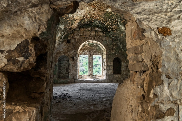 Fototapeta Abandoned stone structure with arched windows, weathered walls, and scenic forest landscape visible through the opening, historic mysterious atmosphere. Lifta, Israel
