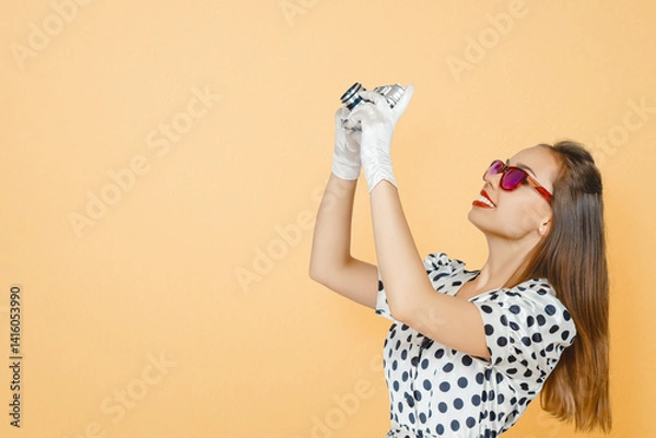 Fototapeta Smiling Brunette Woman Holding a Vintage Camera Against Peach Background, Capturing Memories, Exploring Photography, and Cherishing Nostalgia