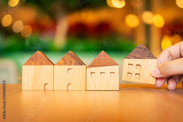 Fototapeta Hand choosing mini wood house model from model on wood table, selective focus, Planning to buy property. Choose what's the best. A symbol for construction ,ecology, loan concepts	