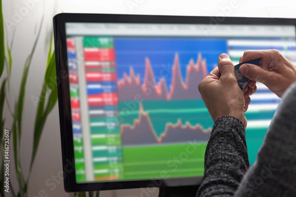 Fototapeta Closeup of male hands tearing credit card on the background of computer monitor with charts. Man trading stocks on monitor, back view, charts visible. Payment card destruction in progress