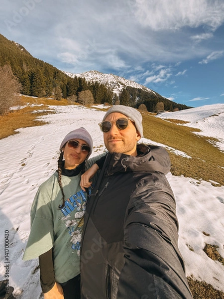 Fototapeta Tourists enjoying winter holidays in a snowy mountain landscape, capturing a selfie against a backdrop of snow-capped peaks and alpine scenery