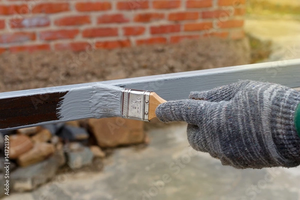 Obraz Gloved hand painting primer anti rust on steel poles for construction. Half - painted surface. Smear of paint brush.