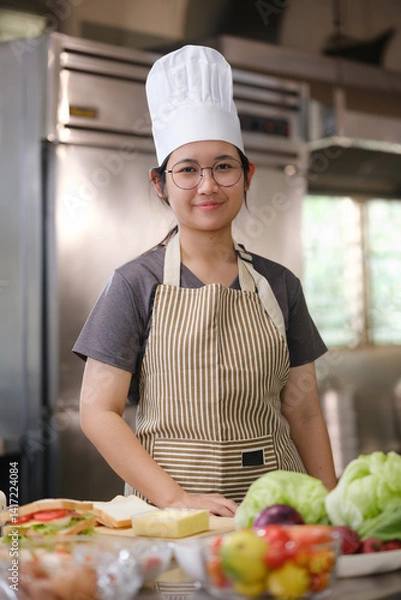 Obraz Culinary student standing confidently in training kitchen with fresh ingredients ready for cooking practice