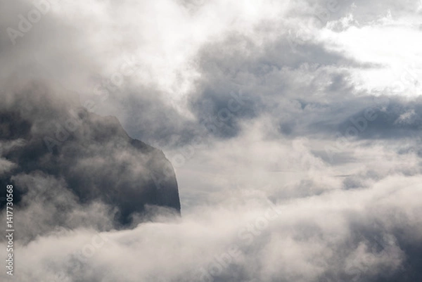 Fototapeta Panorama of a rugged mountain exposed between mist and clouds with partially transparent sky