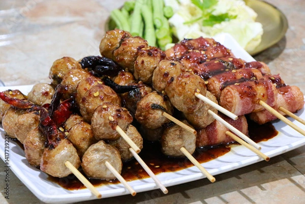 Fototapeta Grilled Meatballs. fish ball and sausage hotdog grilled in stick on tray, Fried pork meatballs skewers bamboo on a white plate with spicy sauce on a table, Thai street food.