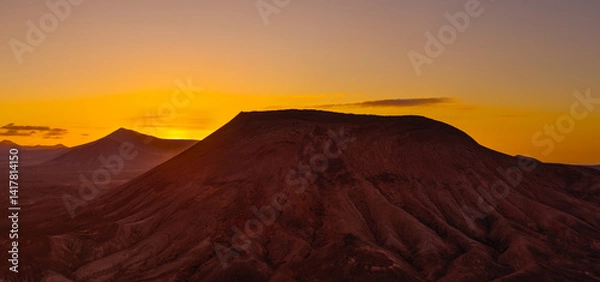 Obraz Beautiful aerial sunset image over Montana Roja volcanic crater silhouetted against the setting sun and skyscape near Corralejo, Fuerteventura, Canary Islands, Spain
