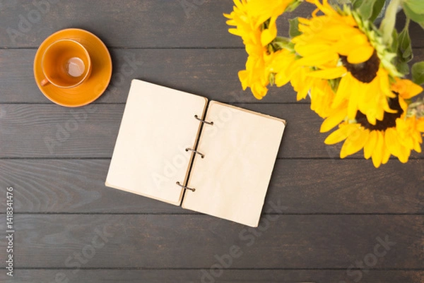 Fototapeta Open notebook with bouquet of sunflowers and empty brown cup on wooden table