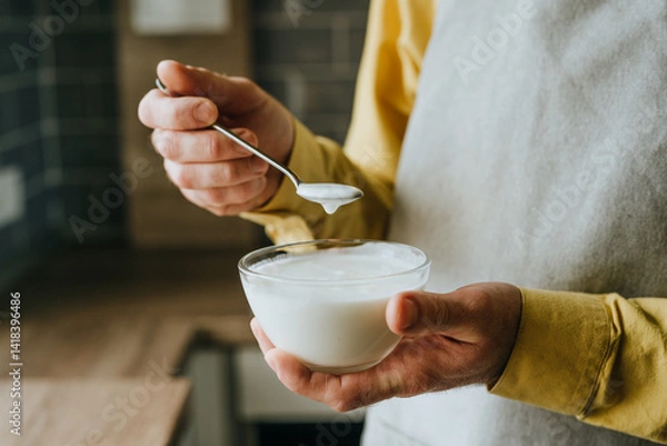 Fototapeta Close-up of man wearing a yellow shirt and an apron holding yogurt in a bowl