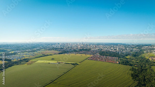 Obraz Wide aerial view of Cascavel, Paraná, Brazil, with agricultural fields and forest in the foreground and a dense urban skyline in the background.