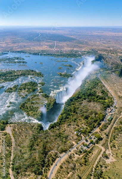Fototapeta The Victoria falls is the largest curtain of water in the world (1708 m wide). The falls and the surrounding area is the National Parks and World Heritage Site (helicopter view) - Zambia, Zimbabwe
