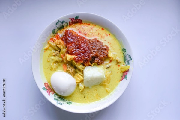 Fototapeta Lontong, a traditional Southeast Asian dish of compressed rice cakes in rich coconut curry, served with lodeh, sambal kacang, sambal tumis, hard-boiled eggs, and fresh vegetables on a decorative plate