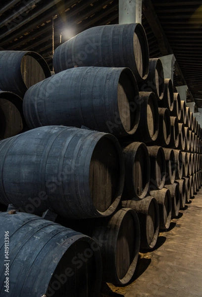 Obraz Close-up of rows of dark wood wine barrels stacked in a wine cellar for aging dark wines and spirits in low light to preserve their quality.