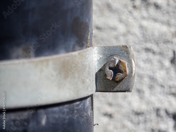 Obraz Close-up of a metal clamp securing a pipe against a textured wall.