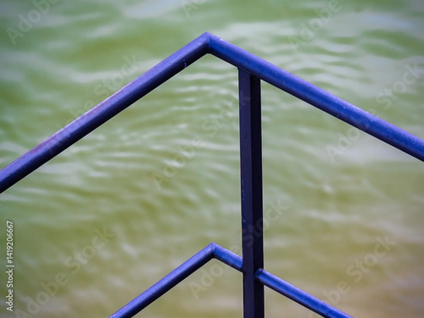 Obraz Close-up of a blue metal railing against a green water background.