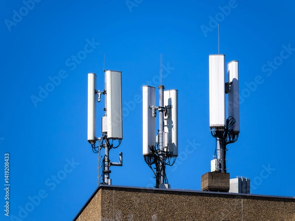 Obraz Three cellular antennas mounted on a rooftop against a clear blue sky.