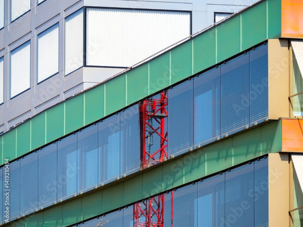 Obraz Modern building facade with colorful panels and glass windows,  red construction crane reflection