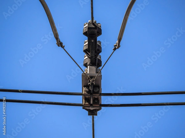Obraz Close-up of a tram or trolleybus overhead power line against a clear blue sky.