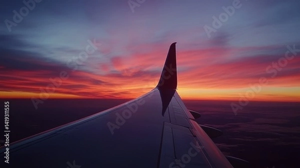 Fototapeta The wing of an airplane is captured during a radiant sunset flight, providing a spectacular view of the horizon painted with the breathtaking colors of dusk
