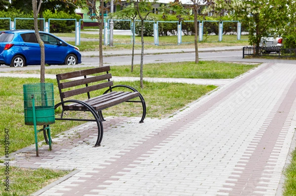 Fototapeta Rest area with bench surrounded by trees and ornamental shrubs in Kyiv, Europe. Place to rest in the city park at summer