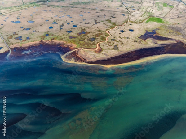 Obraz Aerial shot of a coastal plain filled with blue ponds, a winding river, and colorful sediments flowing into the turquoise sea, forming a natural abstract masterpiece.